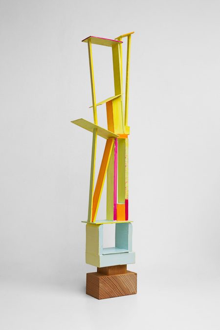 Artwork by Rowan Mace. A tall, thin sculpture made of slats of wood painted in luminous yellow and pink.