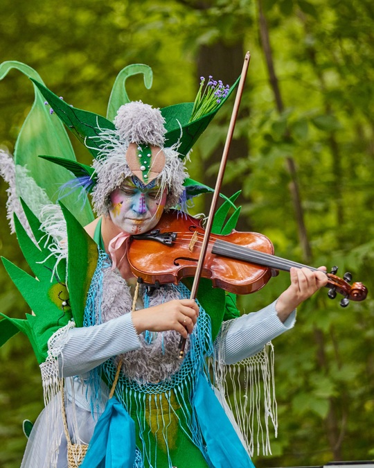 A performer dressed as a fairy plays a violin.