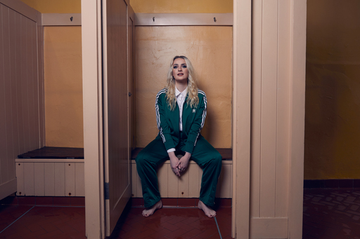 Amy Matthews, sitting on a wooden bench, wearing a green tracksuit.