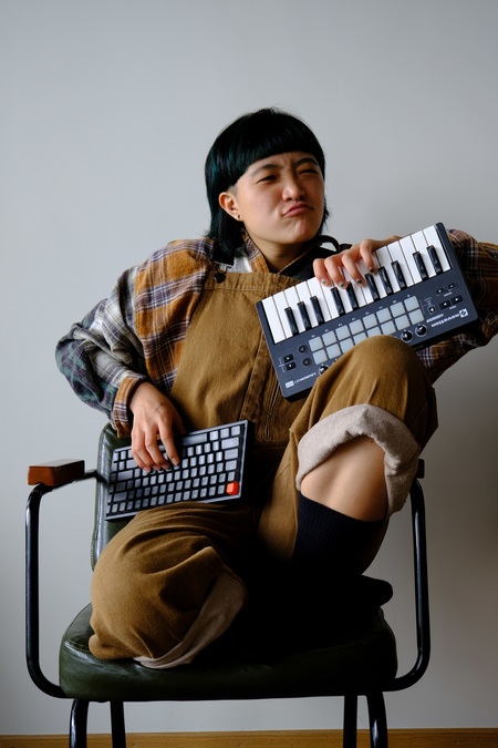 Portrait photo of sarya, sitting in a chair holding a pair of keyboards.