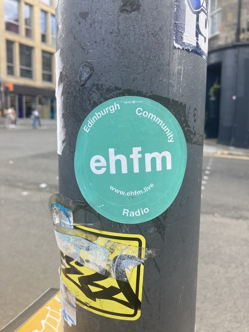A lamppost with a teal sticker in its centre. Text on the sticker reads: 'ehfm, Edinburgh community radio'