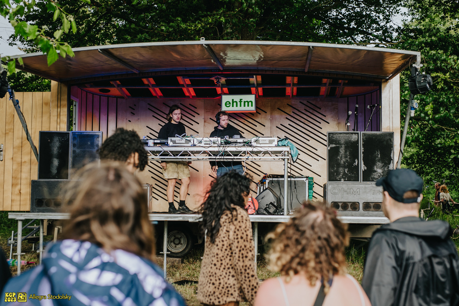 Two DJs perform from a raised stage in front of a crowd. An EHFM branded lightbox can be seen behind the DJ booth.