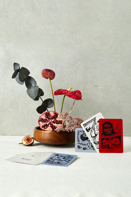 A still life photograph with playing cards, plants, a fig, and a pomegranate.