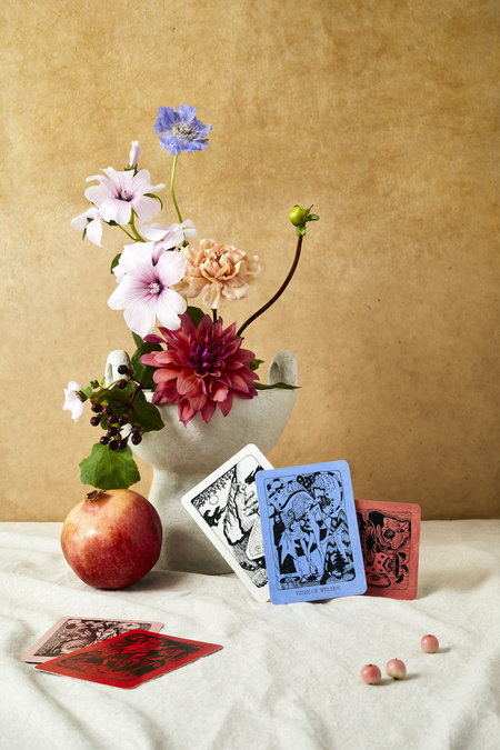 A still life photograph with flowers, playing cards and pieces of fruit.