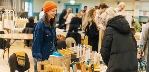 A woman in an orange hat and blue jacket stands behind a market stall full of candles.