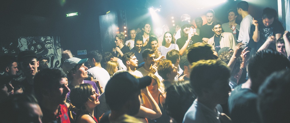 A nightclub crowd, with the DJ booth on the right.