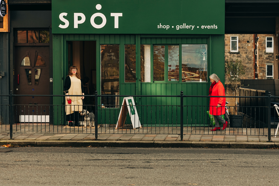 Exterior photo of SPOT design shop; the shopfront is a bright green, and a woman stands outside with her dog.