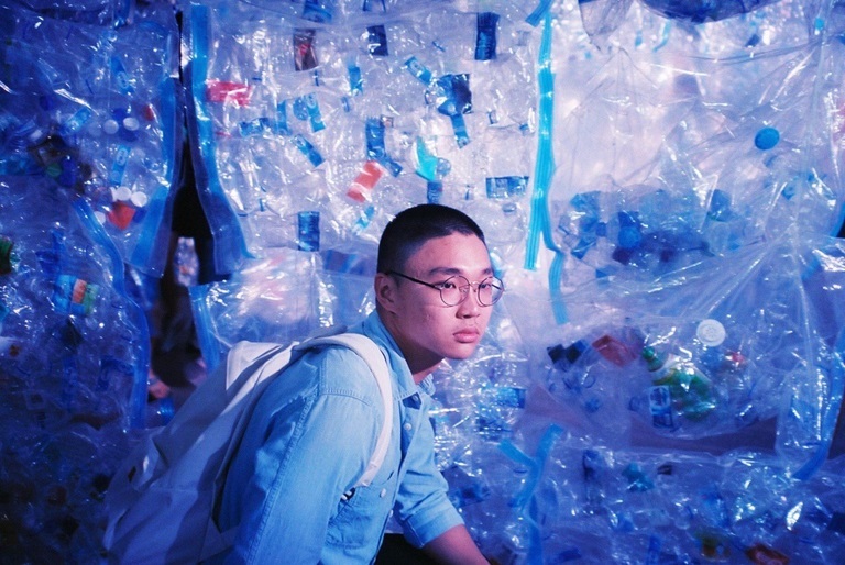 Photo of Jin Hao Li, in front of a wall of plastic bottles and bags.