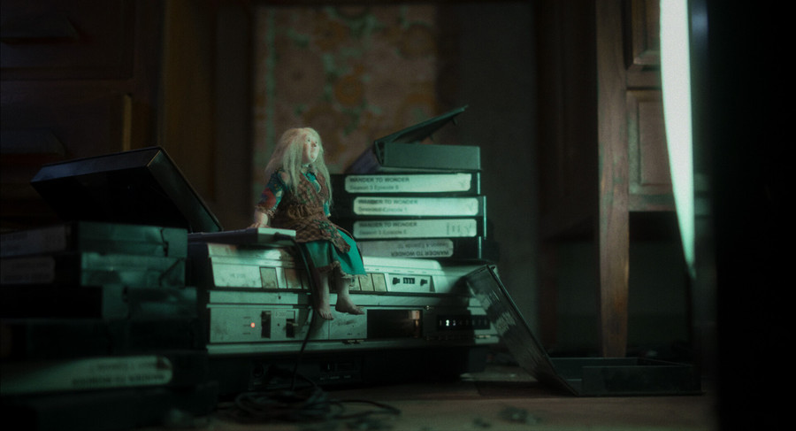 A still from short film Wander to Wonder. An action figure of a woman sits on top of a video recorder, looking at a screen.