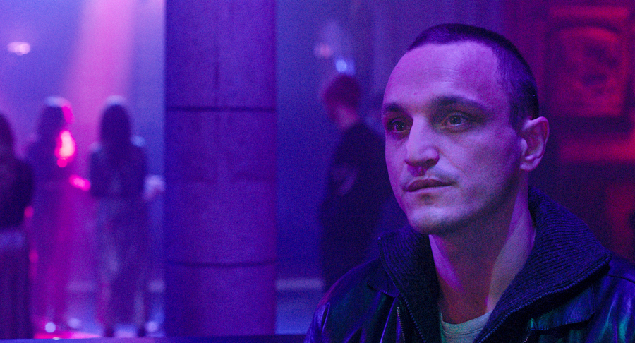 Franz Rogowski sits in a purple-lit nightclub in a scene from the film Disco Boy.