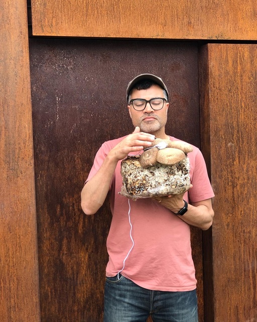 Photograph of Brian D'Souza, holding a large block of mycelium and mushrooms.
