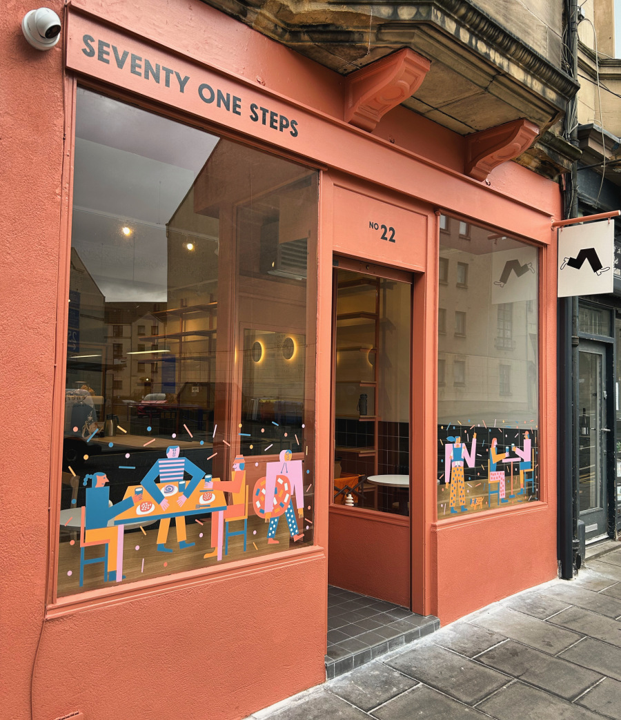 Exterior photograph of Seventy One Steps. A cafe in the ground floor of a tenement building; the exterior is painted in terracota, with blue and yellow decals on the windows.