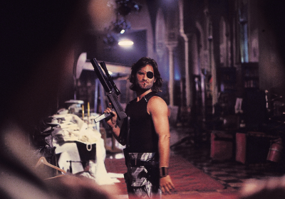 A still from Escape From New York. Kurt Russell stands in an alleyway, holding a gun.