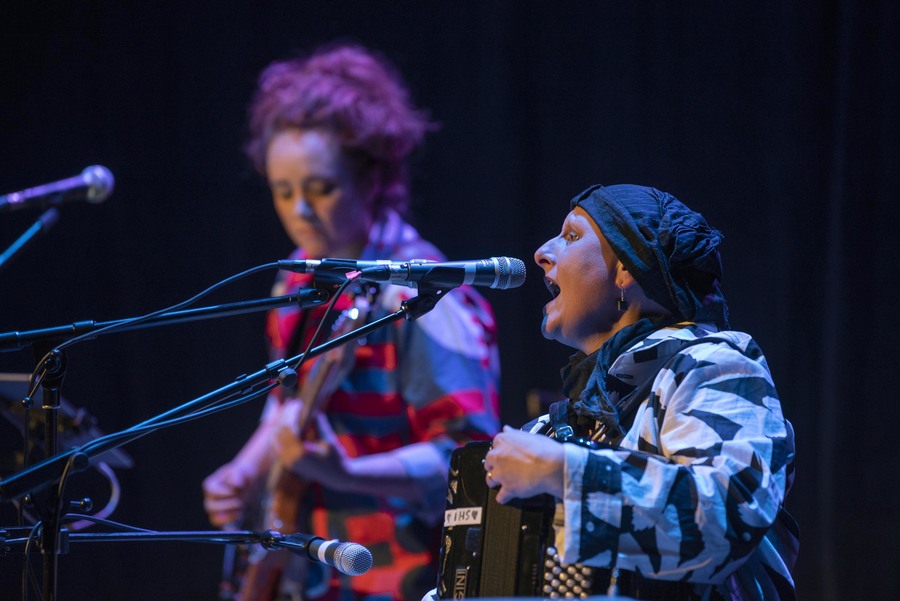 Photo of two members of Birdvox performing. A woman plays an accordion and sings, while a second woman plays guitar in the background.