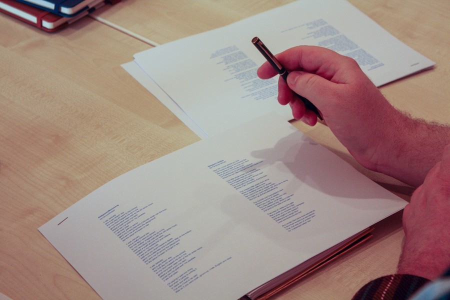 Photo of a page of printed text, with a hand and pen in the top right corner.