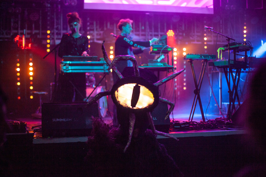 Photo of Maranta performing on stage, with a costumed figure with one illuminated eye standing in front of the band.