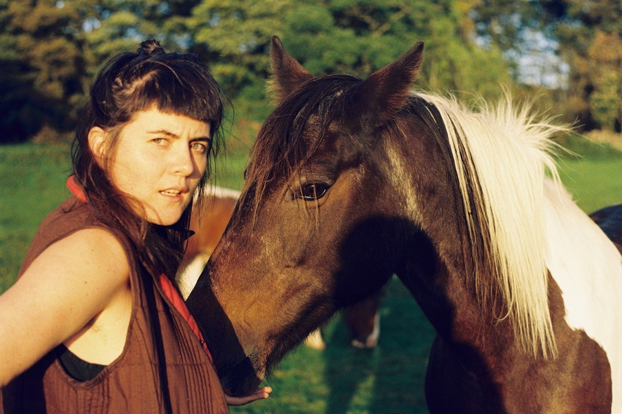 Photo of the musician Quinie, standing next to a brown horse.