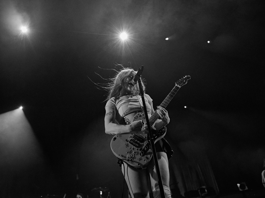 Black and white photo of Rhian Teasdale of Wet Leg singing and playing the guitar.