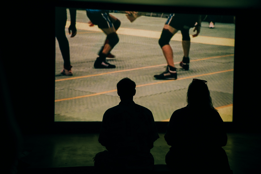 Photo of two people sitting on a gallery bench watching a film as part of the exhibition The Ring In The Fish.