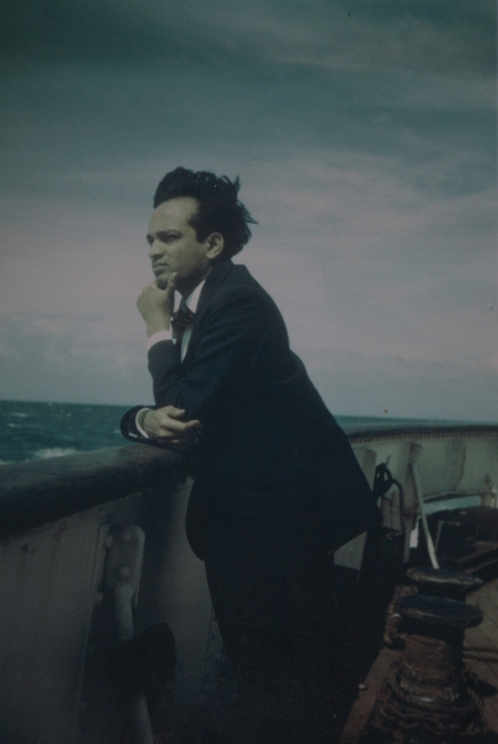 A photo of Syed Ali Ahmed, leaning on a low wall and looking out onto a body of water.