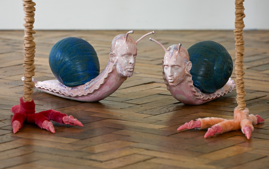 Photo of two sculptures, showing snail-like figures with human faces.
