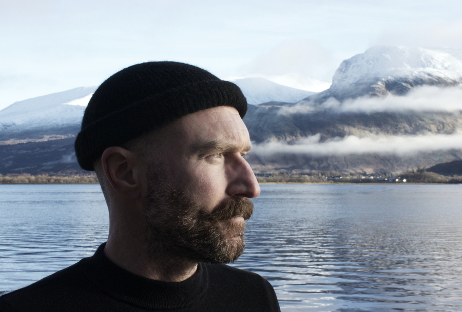 Photo of Lomond Campbell standing in front of a loch and mountains.