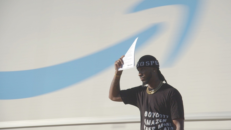 A still from Union; a Black man holds a piece of paper above his head, while standing in front of a painted mural of clouds and sky.