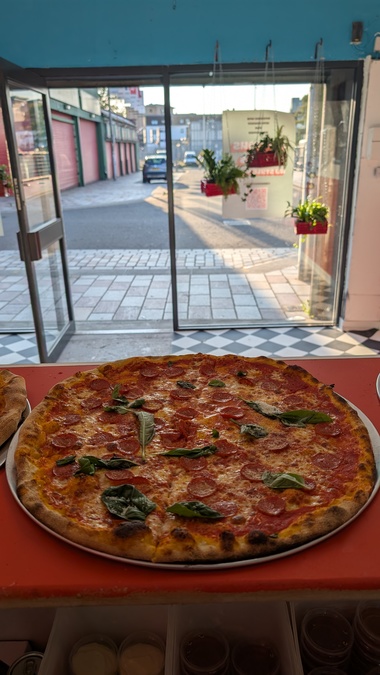 Photo of a large pizza, in front of a glass shopfront.
