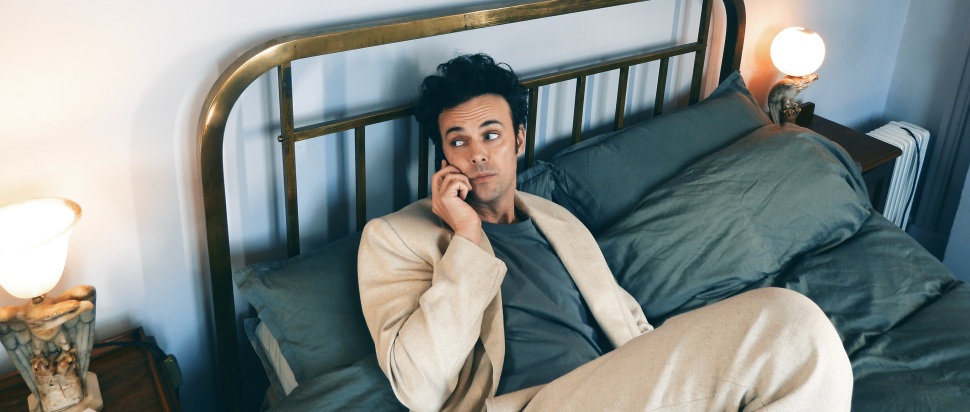 Photo of Rudi Zygadlo, sat on top of a bed holding a phone to his ear.