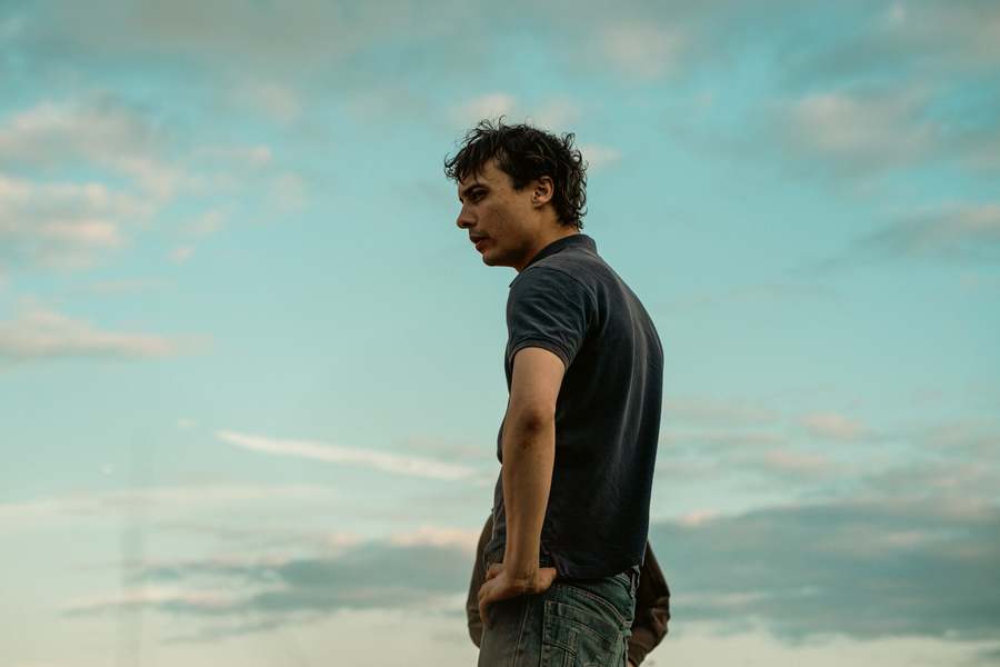 Photo of Frank Dillane in a scene from Urchin, standing with his hand on his hip in front of a cloudy sky.