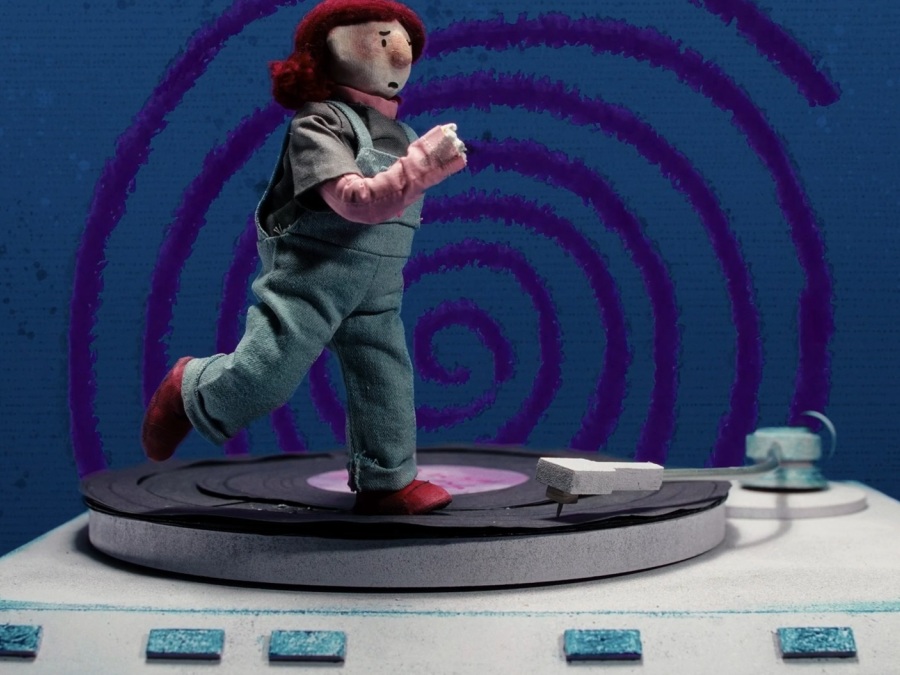 A film still showing a stop motion puppet running against a swirling background.