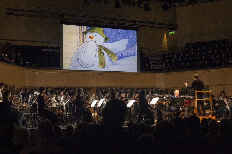 Photo showing the Royal Scottish National Orchestra performing, while the animated film The Snowman plays on a screen behind the orchestra.