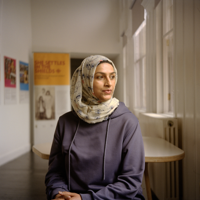 A portrait photograph of a woman in a lilac hooded top and a white patterned headscarf.