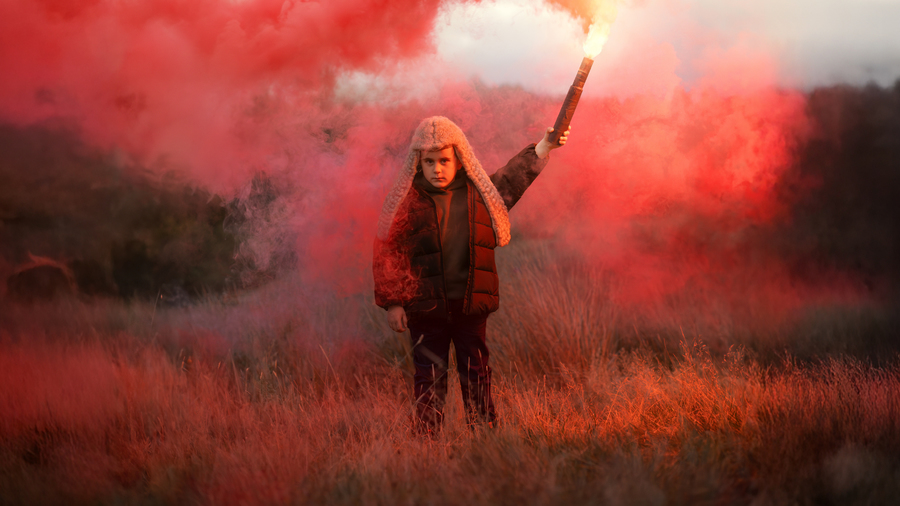 Photograph of a small child holding a lit red flare above their head.