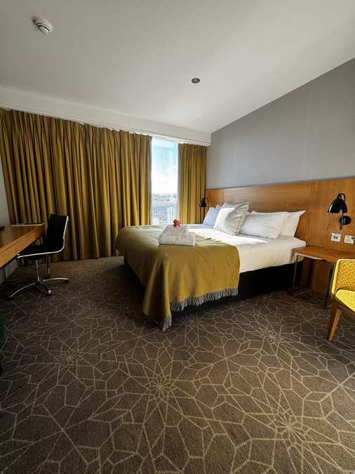 Photograph of a hotel room, with a bed, chair, and desk.