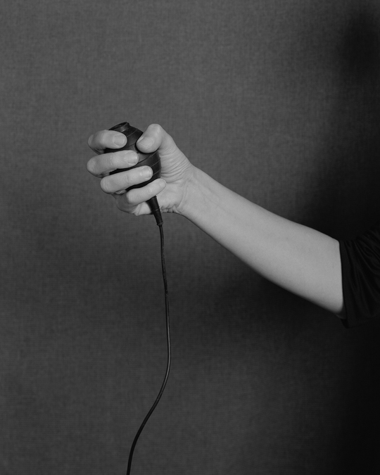 Black and white photo of an arm reaching out from behind a curtain, holding a camera timer.