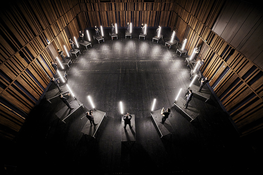 Overhead photo of a group of pipers standing in a circle in a large darkened room.
