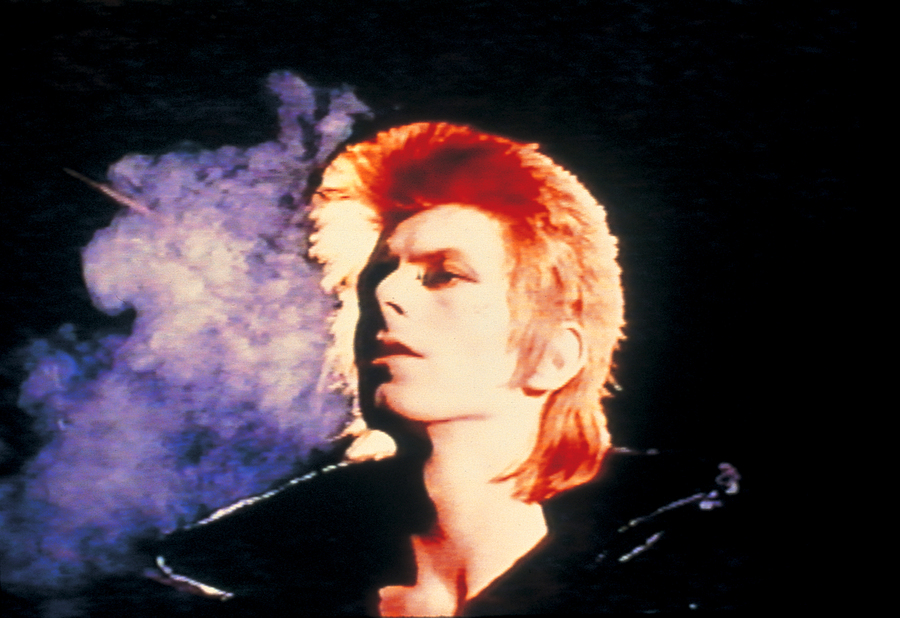 A still from the music video for John I'm Only Dancing by David Bowie. Bowie stands in the middle of the frame in a jacket with a large collar.