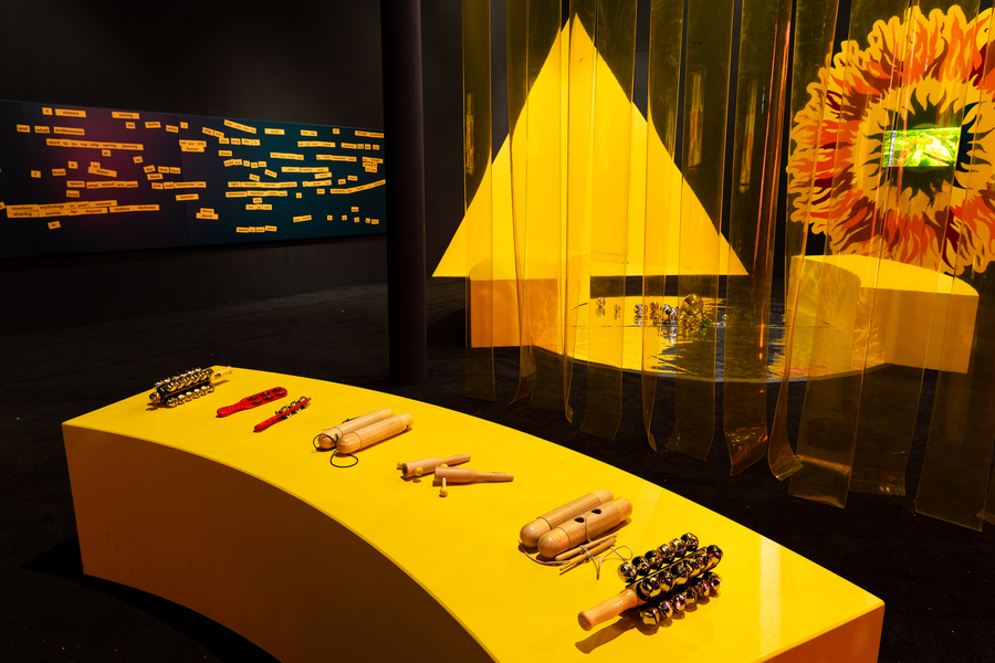 A photo of The Mothership Collective 2:0 exhibition, with a yellow bench covered in handheld musical instruments.